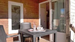 Eine überdachte Terrasse mit Korbmöbeln, einem Glastisch und einer Tür zu einem Innenraum.