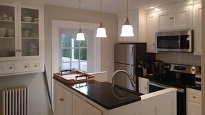 Una cocina moderna con armarios blancos, un refrigerador de acero inoxidable, un microondas e iluminación colgante.