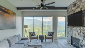 A spacious living room with a large window offering a mountain view, a stone fireplace, and a ceiling fan.