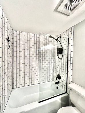 Een moderne badkamer met een douchecabine van glas, witte betegelde wanden en een wit toilet.