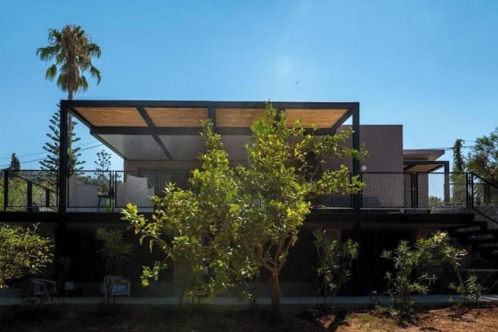 Um edifício moderno com telhado plano, grandes janelas e área externa coberta.