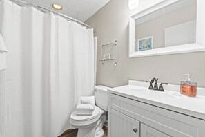 Ein Badezimmer mit Toilette, Waschbecken mit Seifenspender und Duschvorhang.