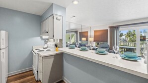 Una cocina moderna con electrodomésticos blancos, una encimera con vajilla azul y vistas al exterior a través de ventanas amplias.