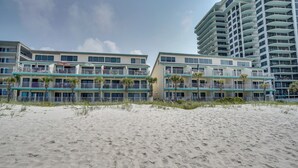 Un hotel frente a la playa con varios balcones, palmeras y una playa de arena.