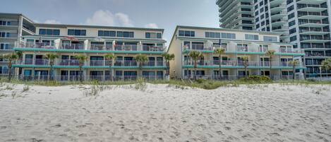 A beachfront hotel with multiple balconies, palm trees, and a sandy beach.