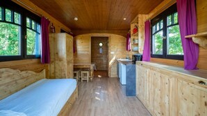 Una cabaña con interior de madera, una cama, un pequeño rincón de cocina y una mesa de comedor.