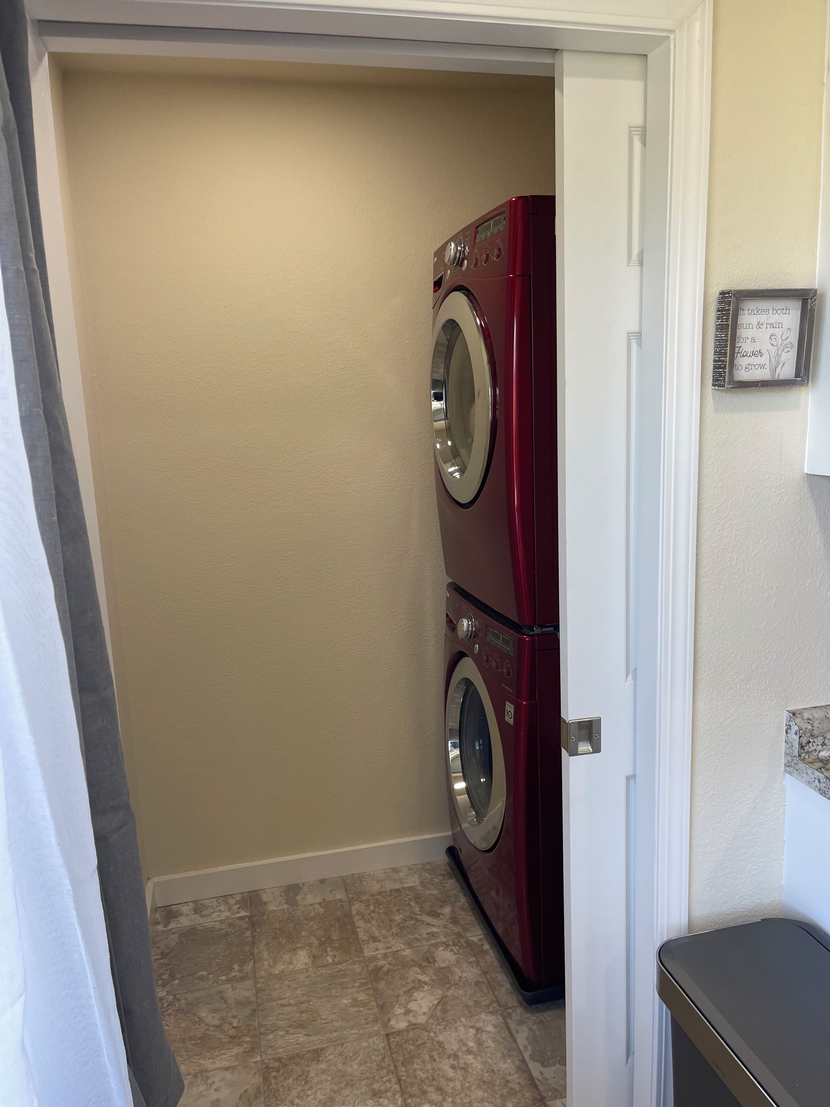 A laundry room with two stacked front-loading washers and dryers, beige walls, and a tiled floor.
