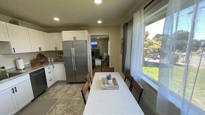 A modern kitchen with white cabinets, a stainless steel refrigerator, and a dining area with a table and chairs.