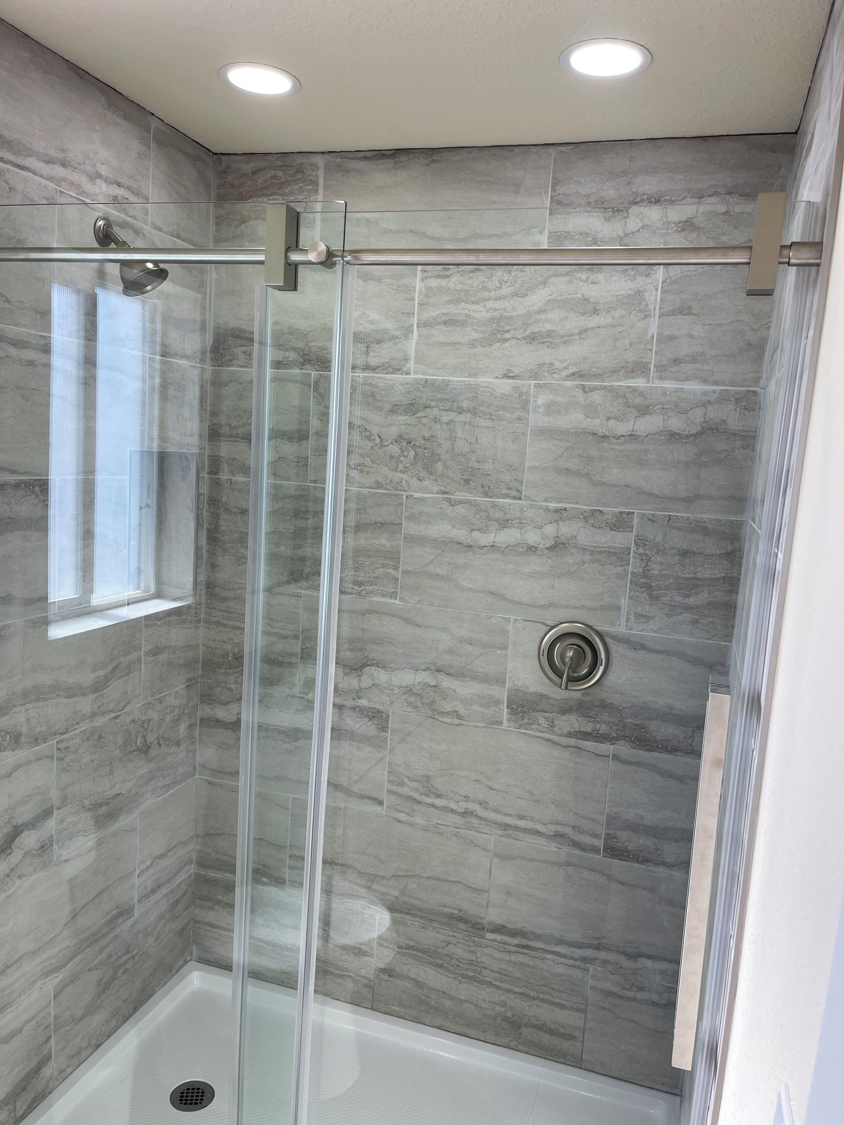 A modern shower with a glass door, a window, and a built-in hand dryer.