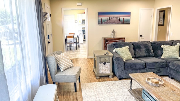 A living room with a grey sofa, a white table, and a wooden coffee table. There is a painting on the wall and a lamp on a side table.