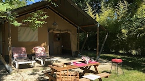 A rustic outdoor seating area with a picnic table, lounge chairs, and a small red stool. - ZEcamping 4 étoiles avec pataugeoire et piscine - animaux acceptés (Meyronne)