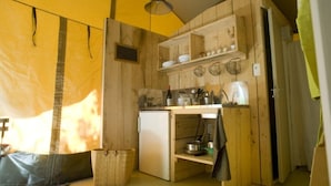 A compact kitchen with wooden cabinets, a refrigerator, and a hanging light fixture. - ZEcamping 4 étoiles avec pataugeoire et piscine - animaux acceptés (Meyronne)
