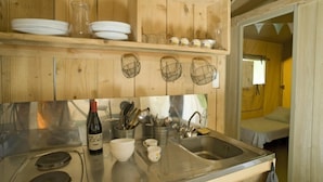 A wooden kitchen with a stainless steel sink, a wine bottle, and utensils. - ZEcamping 4 étoiles avec pataugeoire et piscine - animaux acceptés (Meyronne)