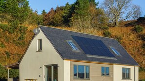 Een modern huis met een schuin dak, zonnepanelen en een klein terras.