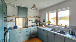 Een moderne keuken met grijze kastjes, een RVS spoelbak en een raam met uitzicht op de omgeving.