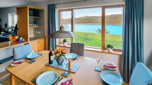 Een eetruimte met een tafel voor vier personen, uitzicht op een meer en een keuken op de achtergrond.