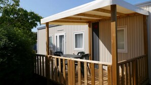 A mobile home with a wooden deck, two windows, and a table with chairs.