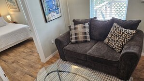 A living room with a dark grey sofa, two patterned cushions, a glass coffee table, and a wooden floor. - Gull Wing * No Stairs! * Downtown * Beautiful (Cedar Key)