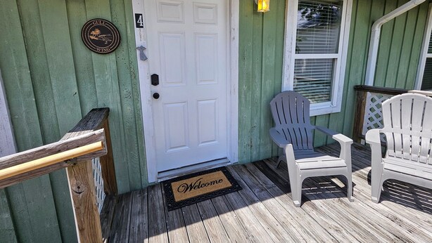 A wooden porch with a white door, two Adirondack chairs, and a welcome mat. - Gull Wing * No Stairs! * Downtown * Beautiful (Cedar Key)
