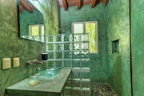 Un baño con lavamanos de vidrio, un espejo y una ventana.
