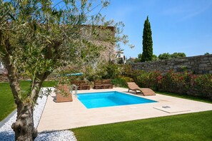 Una piscina con sillones de descanso, un muro de piedra y un árbol.