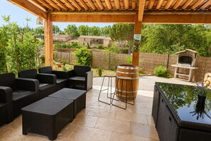 Un patio al aire libre con mobiliario de mimbre, un taburete de barril de madera y una parrilla para barbacoa de piedra.