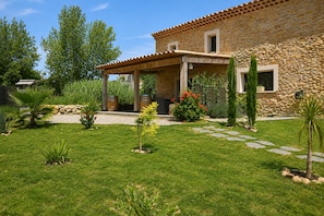A stone building with a covered patio, a well-maintained lawn, and various plants.