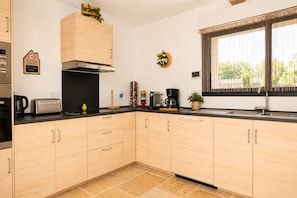 Una cocina moderna con armarios de madera, horno empotrado, cafetera y una ventana con cortinas.