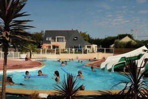 Ein Schwimmbad mit Personen, einer Rutsche und einem Haus im Hintergrund.