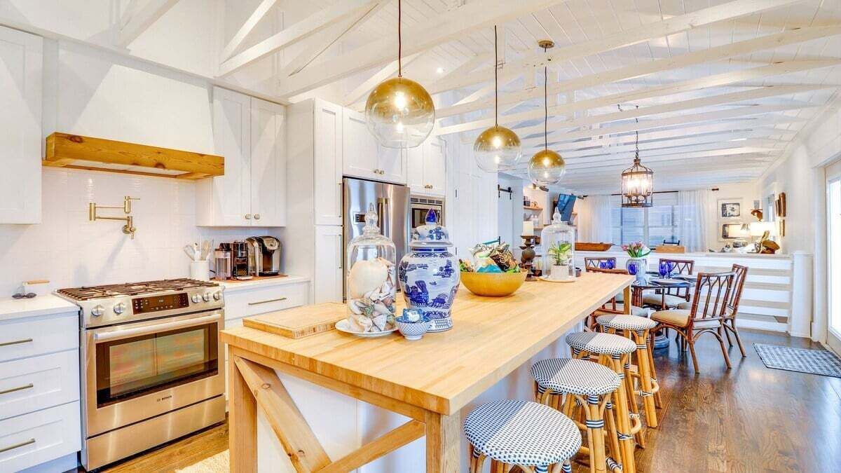 Cozinha moderna com ilha de madeira, eletrodomésticos de aço inoxidável e luminárias pendentes.