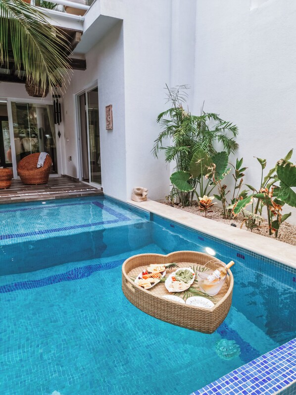 A swimming pool with a floating basket containing food and drinks, surrounded by plants and a white wall. - Stunning new villa heated pool, 4 bedrooms, walk to Calle 7, outdoor dining (Tulum)