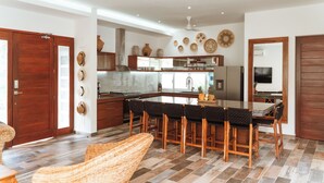 Cozinha espaçosa com ilha central, armários de madeira e área de refeições com uma cadeira de fibra natural.