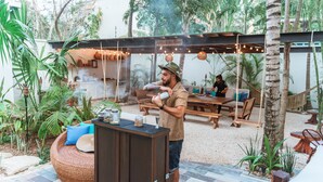 Uma área de pátio ao ar livre com mesa de madeira, assentos de vime e um bar.