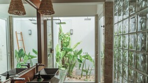 Uma casa de banho com um espelho grande, duas pias, zona de duche e vista para um jardim através de uma porta de vidro.