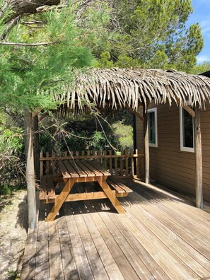 A wooden deck with a picnic table and a thatched-roof structure. - Cabane 3 étoiles - Piscine  - eehdah (Portel-des-Corbières)