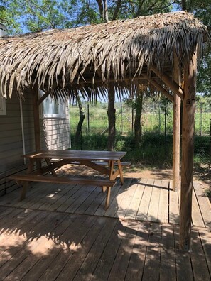 Un patio in legno con tavolo da picnic e una struttura con tetto di paglia.