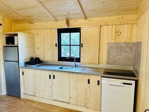 A compact kitchen with wooden cabinets, a refrigerator, a dishwasher, and a window.