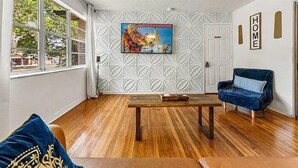 Une pièce avec un plancher en bois, un canapé bleu, une table basse en bois, un tableau au mur et un motif décoratif sur le mur.