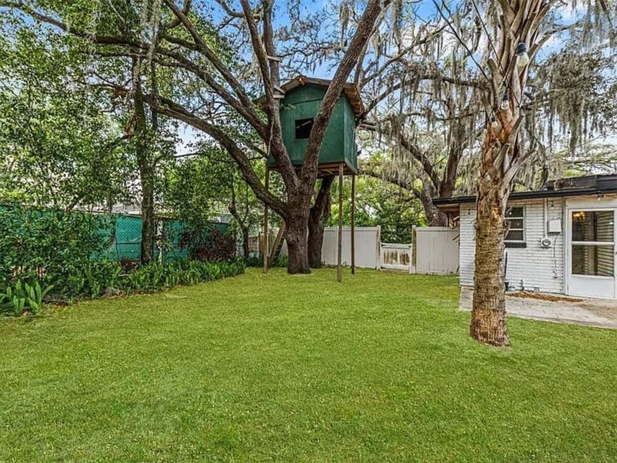 A treehouse attached to a large tree in a well-maintained yard with a house in the background.