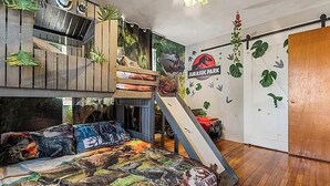 Une chambre avec un lit superposé, un toboggan et une fresque représentant un dinosaure.