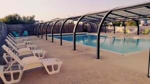 A swimming pool with a covered area, lounge chairs, and a concrete deck.