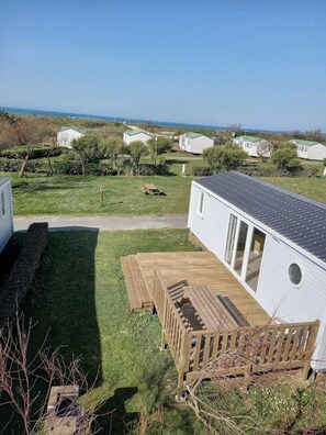 A mobile home with a deck, a grassy yard, and a view of other mobile homes in the background.