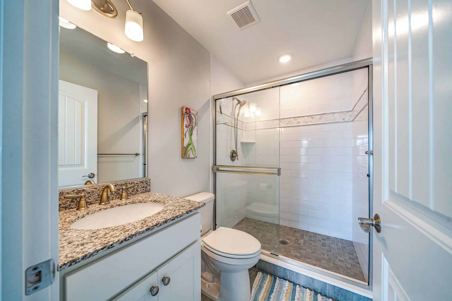 A bathroom with a granite countertop sink, a white toilet, and a glass-enclosed shower.