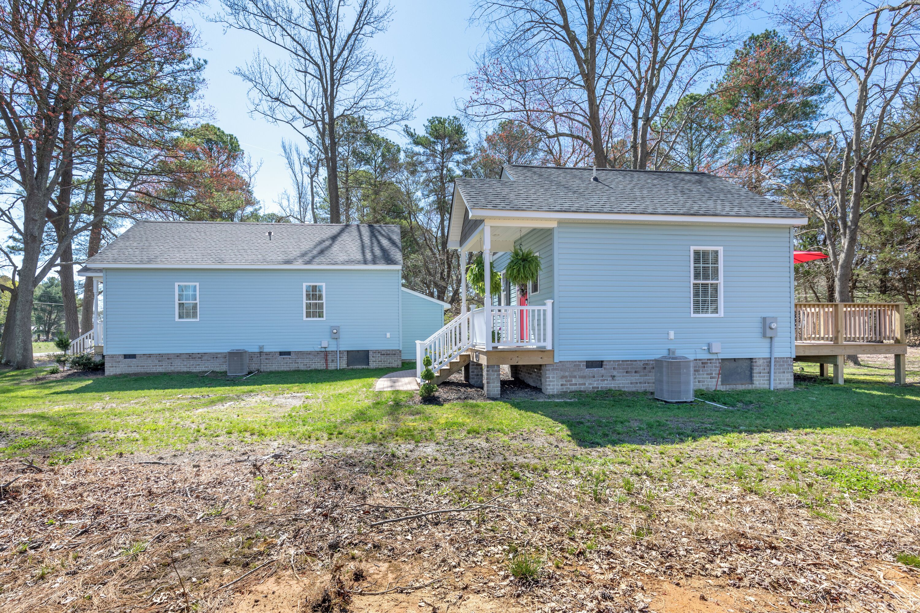 Two single-story houses with a porch and a small deck, surrounded by trees and grassy yard.