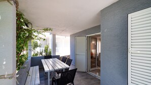 A patio with a wooden table and chairs, a sliding glass door leading to an indoor area, and a wall with a textured finish. - Bbq Holly Garden Novalja D (Novalja)