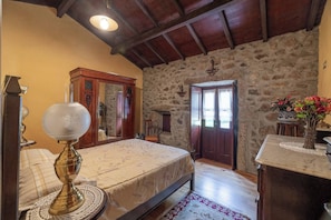 Une chambre à coucher avec un lit, une commode en bois, un mur en pierre et une porte.