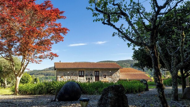 Un edificio de piedra con techo de tejas rojas, rodeado de árboles y un camino de grava.
