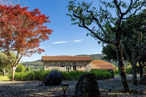 A stone building with a red-tiled roof, surrounded by trees and a gravel path. - Stone House Casa das Pedras (Vila Nova de Cerveira)