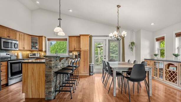 A modern kitchen with wooden cabinets, a stone island, and a dining area with black chairs.