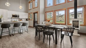 Cocina moderna con armarios blancos, una isla central con taburetes de bar y ventanas amplias que ofrecen vistas al exterior.